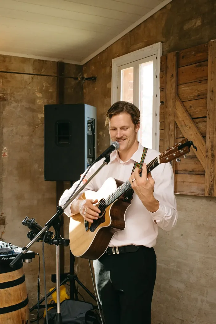 Jem Pryse playing acoustic guitar and singing in a barn