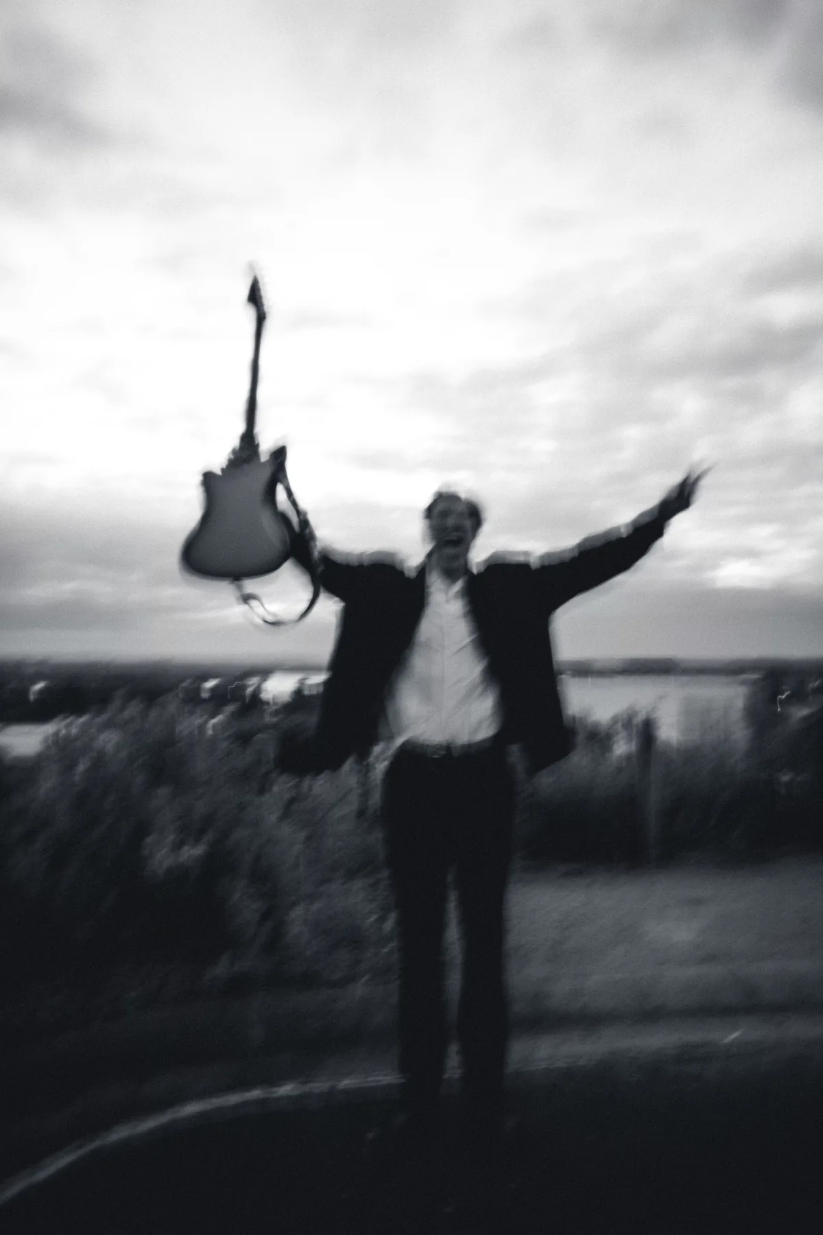 Jem Pryse holding a guitar above his head in a field