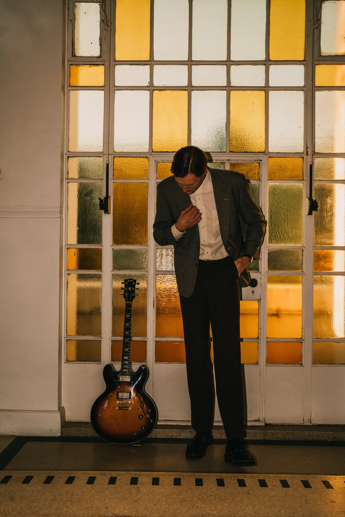 Jem Pryse with a guitar beside a yellow glass door